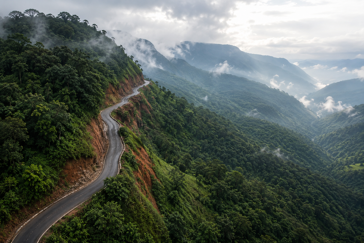 A single sealed road switchbacking down a forested Western Ghats ridge under cloud